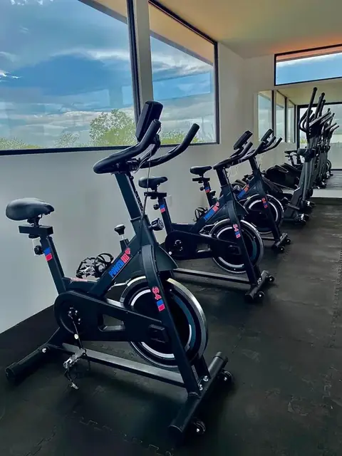 Área de gimnasio interior del club con bicicletas de spinning de última generación frente a ventanales